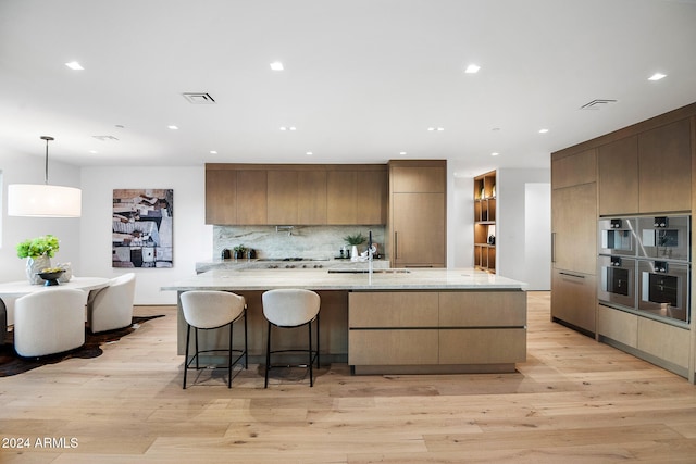 kitchen featuring light stone countertops, sink, hanging light fixtures, light hardwood / wood-style flooring, and decorative backsplash