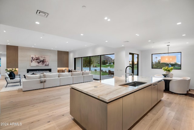 kitchen featuring light stone countertops, sink, a spacious island, light hardwood / wood-style floors, and a fireplace