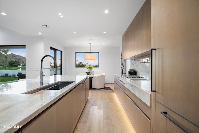 kitchen featuring light stone countertops, sink, light brown cabinets, decorative light fixtures, and light hardwood / wood-style floors