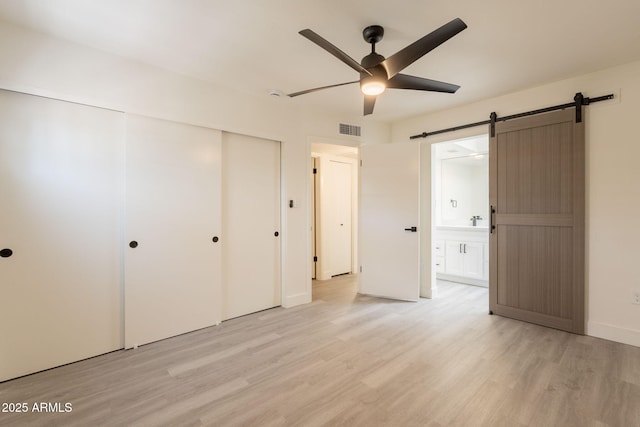 6544 N 7th Ave Unit 14, Phoenix, AZ 85013 - unfurnished bedroom featuring light wood-type flooring, a closet, a barn door, ensuite bath, and a ceiling fan