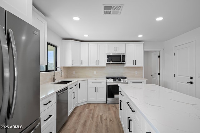 kitchen with visible vents, a sink, decorative backsplash, stainless steel appliances, and light wood-type flooring