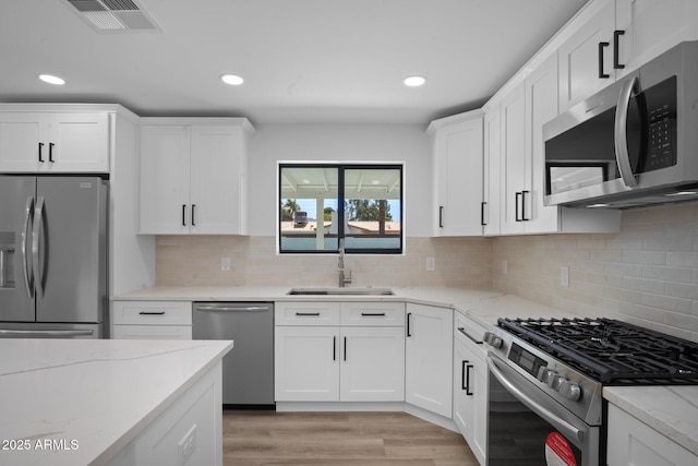 kitchen featuring light wood finished floors, visible vents, appliances with stainless steel finishes, white cabinetry, and a sink