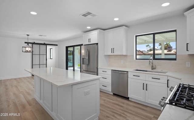 kitchen with visible vents, a kitchen island, a barn door, appliances with stainless steel finishes, and a sink