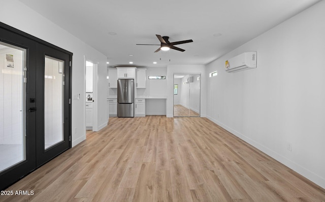 unfurnished living room with an AC wall unit, light wood-style floors, baseboards, and french doors