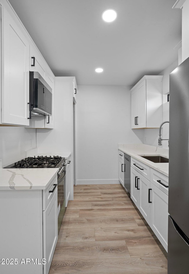 kitchen with a sink, recessed lighting, appliances with stainless steel finishes, white cabinets, and light wood finished floors