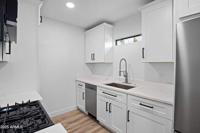 kitchen with light wood-type flooring, a sink, light stone counters, stainless steel appliances, and white cabinets