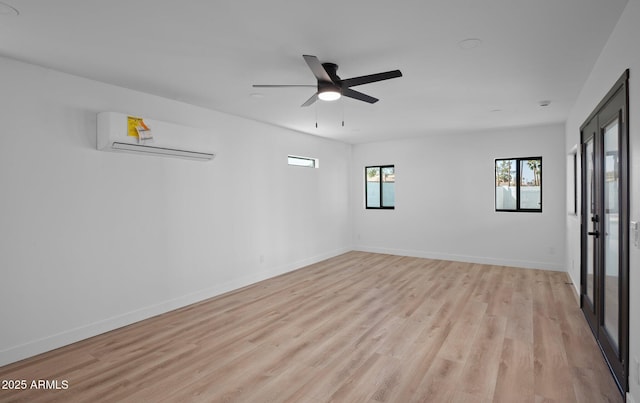 spare room featuring a wall mounted air conditioner, baseboards, light wood-style flooring, and ceiling fan