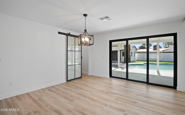 empty room featuring light wood finished floors, visible vents, baseboards, and a barn door