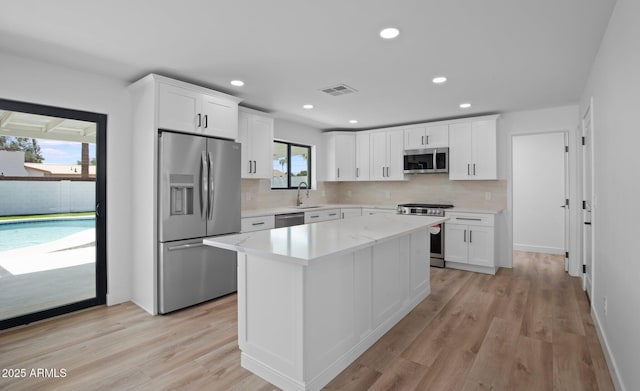 kitchen with tasteful backsplash, white cabinets, appliances with stainless steel finishes, and light wood-style flooring