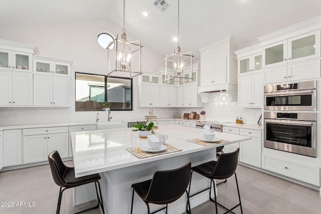 kitchen featuring white cabinets, a kitchen bar, glass insert cabinets, and appliances with stainless steel finishes