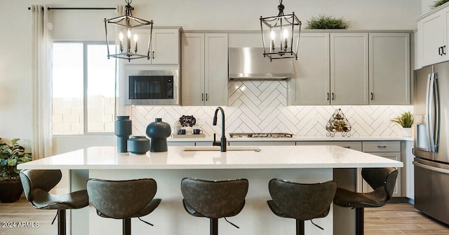 kitchen with black microwave, pendant lighting, an island with sink, and stainless steel fridge