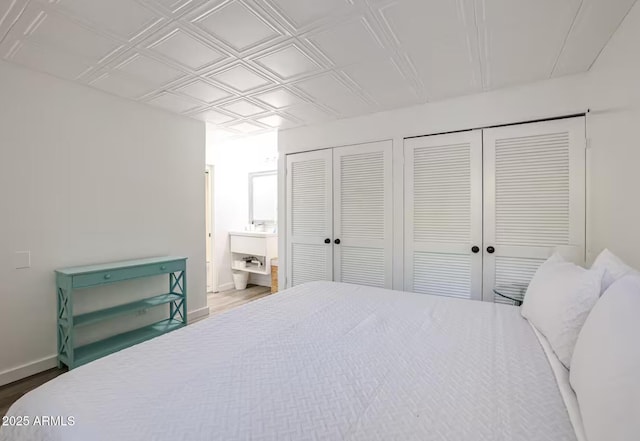 bedroom with multiple closets, wood finished floors, baseboards, an ornate ceiling, and connected bathroom