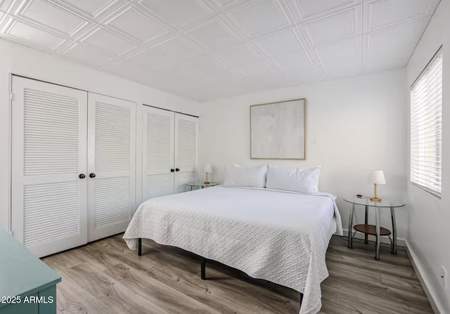 bedroom featuring two closets, baseboards, and wood finished floors