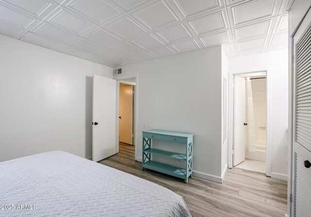 bedroom with visible vents, light wood-style floors, baseboards, an ornate ceiling, and ensuite bath