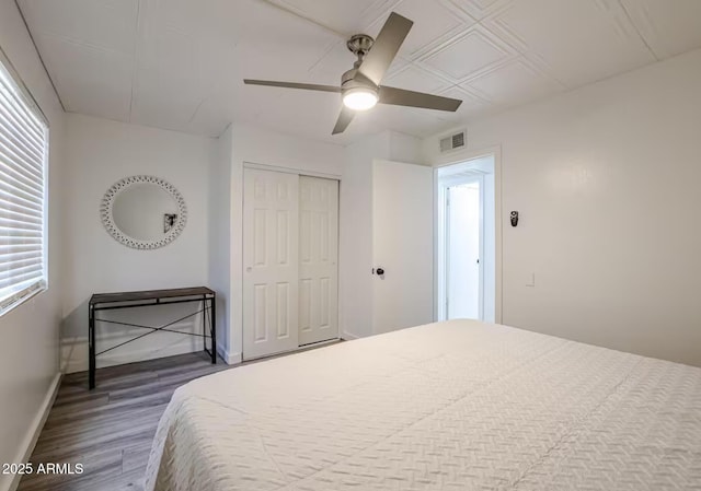 bedroom featuring visible vents, a closet, wood finished floors, baseboards, and ceiling fan