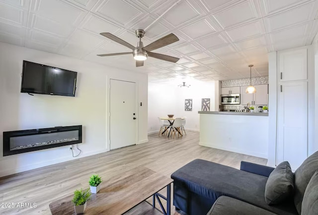 living room featuring an ornate ceiling, ceiling fan, baseboards, and light wood-style flooring