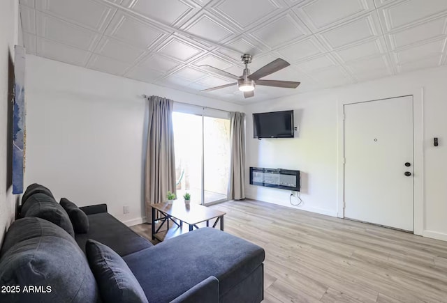 living area featuring light wood-type flooring, a ceiling fan, baseboards, and an ornate ceiling