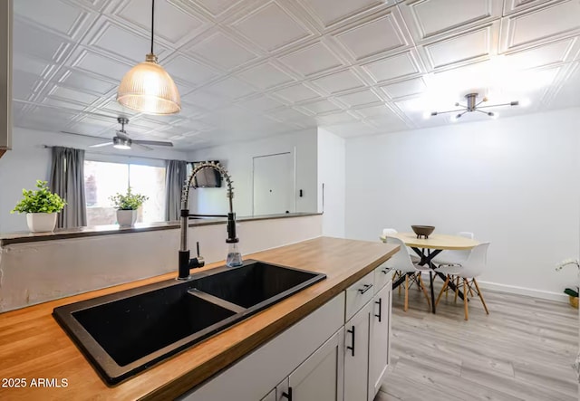 kitchen with ceiling fan, hanging light fixtures, a sink, light wood-style flooring, and butcher block counters