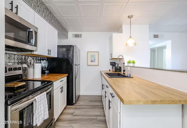 kitchen with appliances with stainless steel finishes, a sink, wood counters, a peninsula, and visible vents