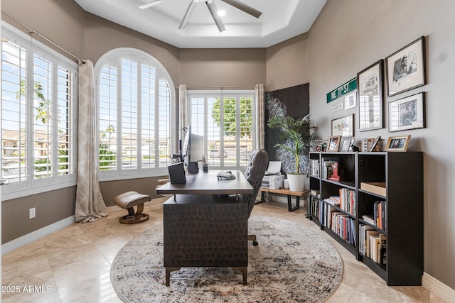 office area featuring a tray ceiling, baseboards, a ceiling fan, and light tile patterned flooring