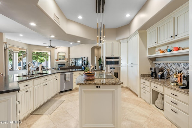 kitchen featuring a kitchen island, decorative light fixtures, stainless steel appliances, open shelves, and a sink