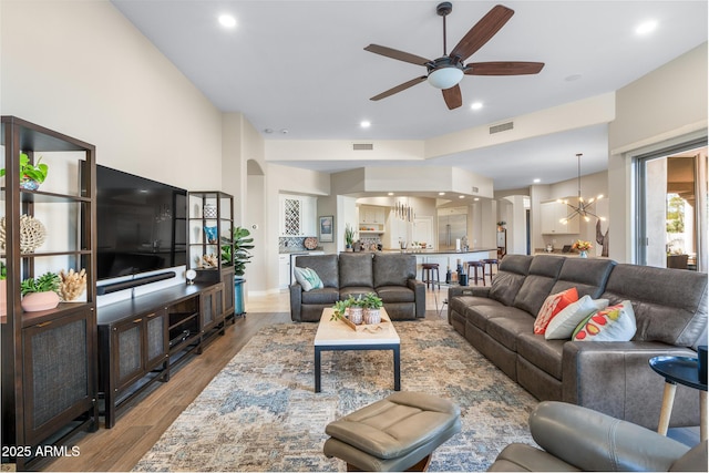 living area featuring ceiling fan with notable chandelier, light wood finished floors, visible vents, and recessed lighting