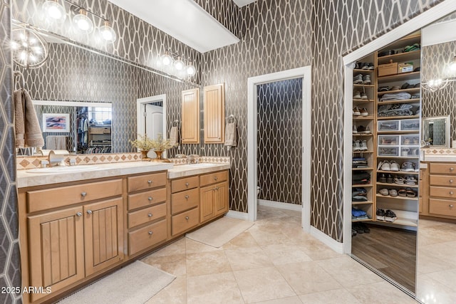 bathroom featuring double vanity, a sink, a spacious closet, and wallpapered walls