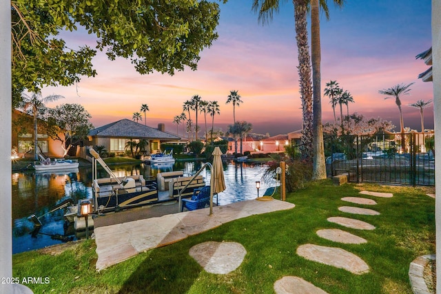 exterior space featuring a water view, a yard, boat lift, and fence