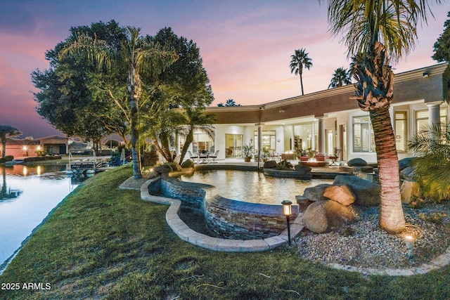 pool at dusk featuring an infinity pool, a yard, and a patio area