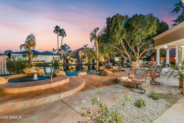 pool at dusk featuring a patio area and a water view