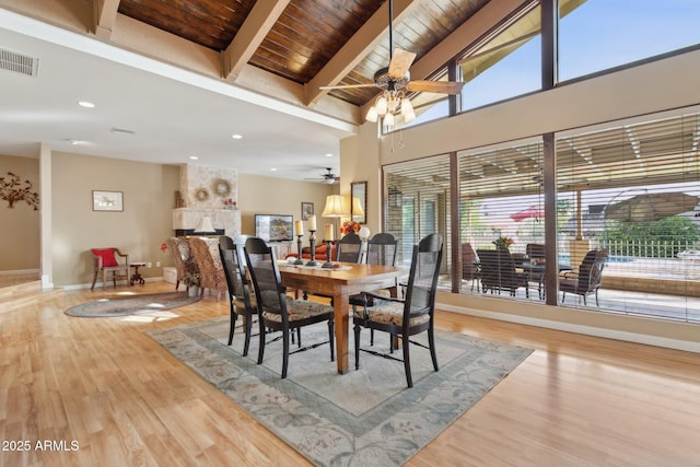 dining room with beam ceiling, visible vents, light wood-style floors, a large fireplace, and baseboards