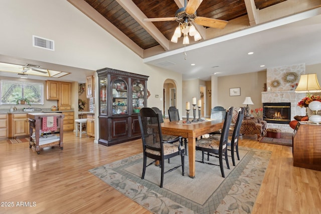 dining room featuring a ceiling fan, visible vents, a stone fireplace, and light wood finished floors