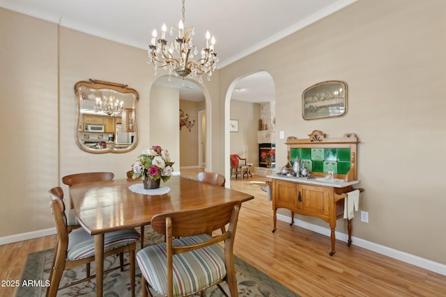 dining area featuring light wood-type flooring, baseboards, a chandelier, and arched walkways