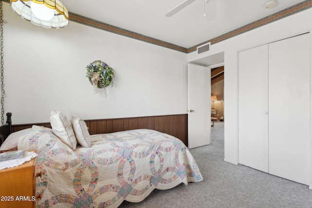 bedroom with a closet, visible vents, ornamental molding, wainscoting, and carpet flooring