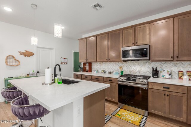 kitchen with light countertops, tasteful backsplash, a sink, light wood-style flooring, and appliances with stainless steel finishes