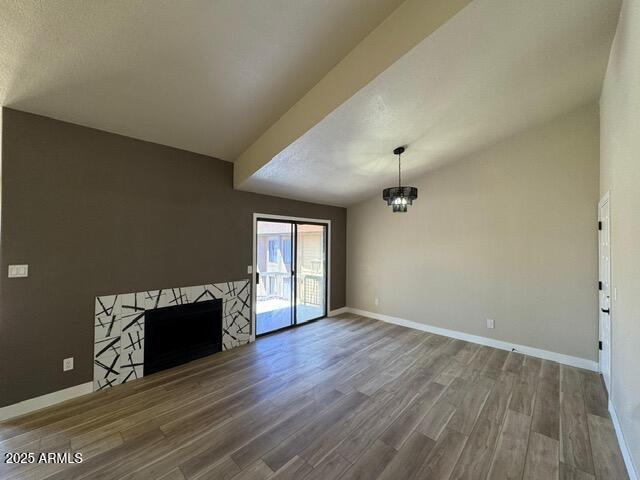 5236 W Peoria Ave Unit 232, Glendale, AZ 85302 - unfurnished living room featuring wood finished floors, a tile fireplace, a chandelier, and vaulted ceiling