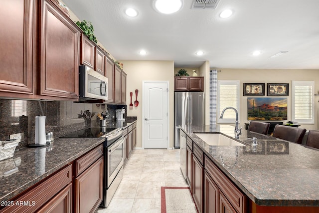kitchen with appliances with stainless steel finishes, a sink, a kitchen island with sink, decorative backsplash, and visible vents