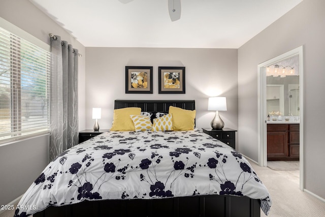bedroom with ceiling fan, light colored carpet, baseboards, and ensuite bath