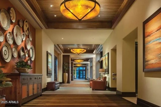 hallway featuring wood ceiling, baseboards, and a tray ceiling