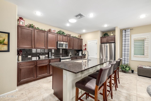 kitchen featuring decorative backsplash, a kitchen breakfast bar, appliances with stainless steel finishes, a sink, and baseboards