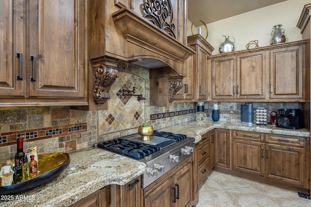 18036 W San Miguel Ave, Litchfield Park, AZ 85340 - kitchen featuring stainless steel gas cooktop, backsplash, light stone countertops, and brown cabinets