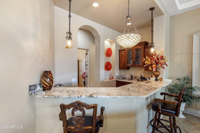 18036 W San Miguel Ave, Litchfield Park, AZ 85340 - kitchen with arched walkways, glass insert cabinets, a peninsula, and light stone counters