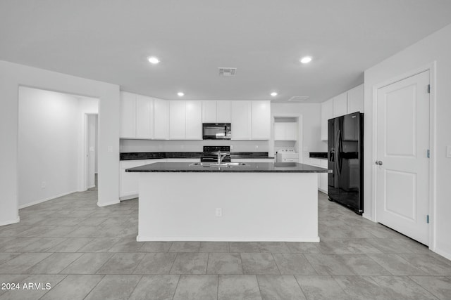 kitchen with white cabinets, dark stone countertops, a center island with sink, and black appliances