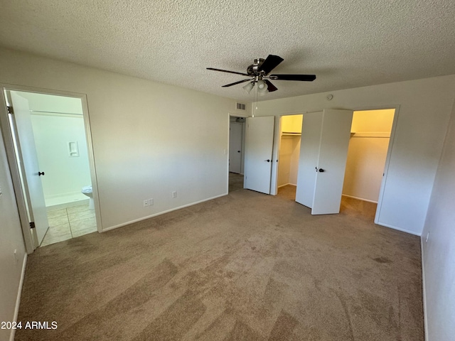 unfurnished bedroom with ensuite bathroom, a spacious closet, a textured ceiling, ceiling fan, and carpet