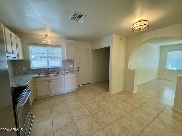 kitchen with light tile patterned floors, backsplash, white cabinetry, light stone countertops, and stainless steel stove