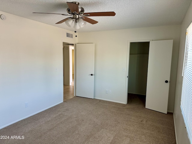 unfurnished bedroom featuring a closet, light carpet, a spacious closet, a textured ceiling, and ceiling fan