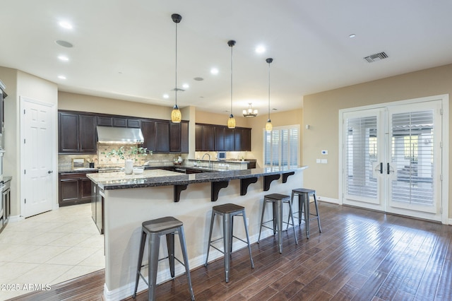 5243 E Windstone Trl, Cave Creek, AZ 85331 - kitchen with a kitchen breakfast bar, under cabinet range hood, dark brown cabinetry, light wood-style floors, and decorative backsplash