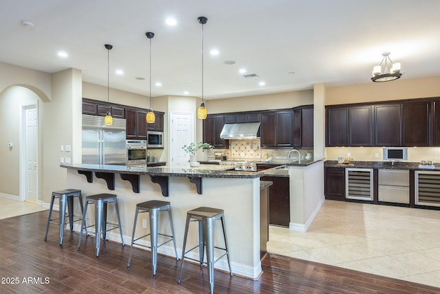 5243 E Windstone Trl, Cave Creek, AZ 85331 - kitchen with under cabinet range hood, built in appliances, beverage cooler, dark brown cabinetry, and recessed lighting