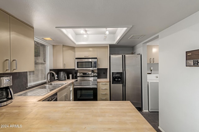 kitchen featuring sink, washer / clothes dryer, cream cabinets, a tray ceiling, and appliances with stainless steel finishes