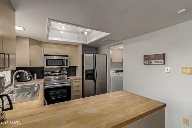 kitchen featuring sink, a raised ceiling, stainless steel appliances, and washing machine and dryer